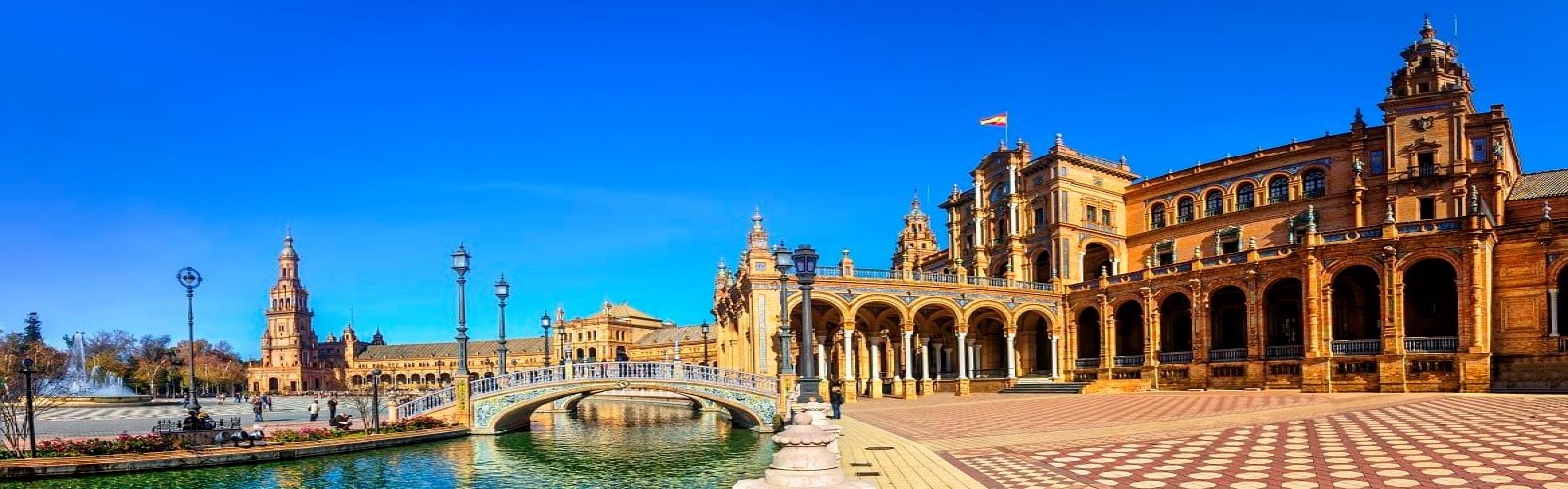 A ground-level view of Seville's Plaza de España, with a small waterway and a large, ornate building featured prominently.